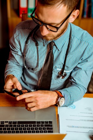 Doctor Observing X-Ray at his Office and using the smartphone. Dramatic scene vivid contrast colorsの写真素材