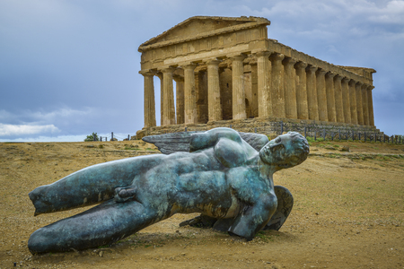 bronze statue of fallen ikaro on the background the concorde temple, Agrigento, Sicily, Italyの写真素材