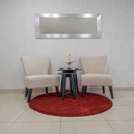 Two chairs stand on a round red carpet mat above a mirror and a small table with decorationの写真素材
