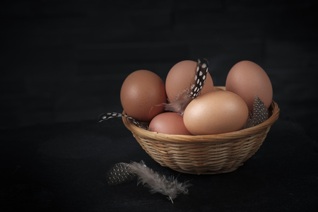 brown eggs in a wicker basket with small feathers set against a black backgroundの写真素材
