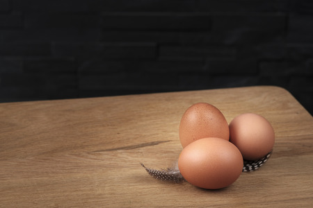 brown eggs on a wooden board with feathers set against a black backgroundの写真素材