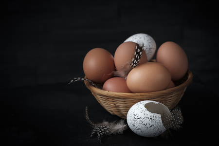 brown and white eggs in a wicker basket with a broken egg in the foregroundの写真素材