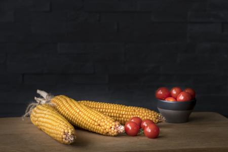 corncob and cherry tomatoes on a wooden chopping board against a dark backgroundの写真素材