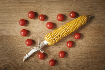 wooden table with tomatoes and corn on the cob in the shape of heart with arrowの写真素材