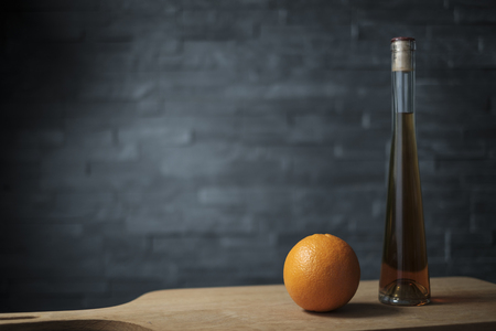 orange with a bottle of liquor on a wooden board against a dark backgroundの写真素材