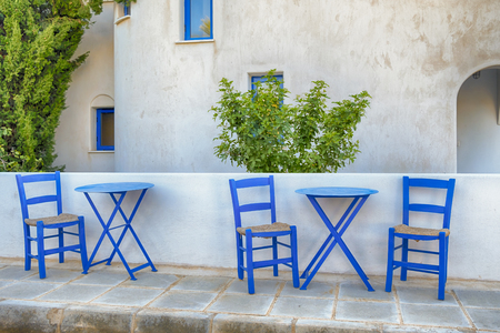 old greek blue chairs with wicker seating on a sun-drenched terrace at a vacation destinationの写真素材