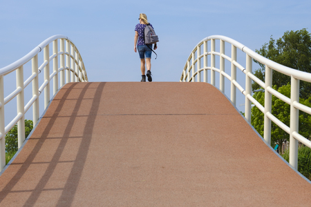 woman with backpack walks on a summer day over a modern pedestrian bridgeの写真素材