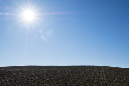bright sun shines in the spring on the plowed field with dark ground and a clear blue skyの写真素材