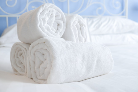 nicely rolled up clean and fresh towels lie on the white sheets of a steel bed in a beautifully lit hotel roomの写真素材