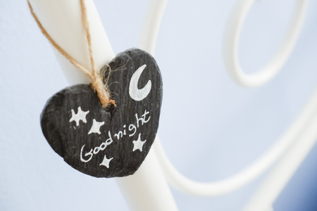 small heart of slate hangs with a rope  as decoration on a steel frame bed with goognight written on it and a drawn moon with starsの写真素材