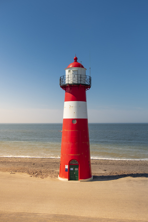 A red and white lighthouse at sea under a clear blue sky near Westkapelle in Zeeland, The Netherlands.の写真素材