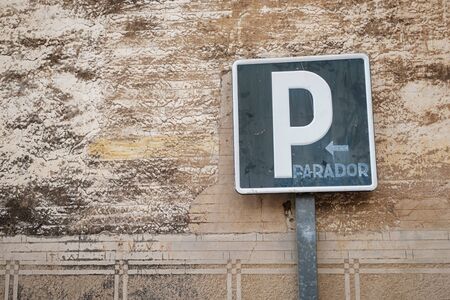 old weathered parking road sign against a stucco old wall with an arrow for the direction and the spanish word parador (parking space)の写真素材