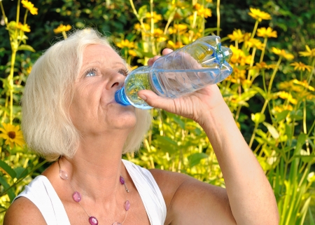 Mature, blonde woman drinking water from bottle in garden の写真素材