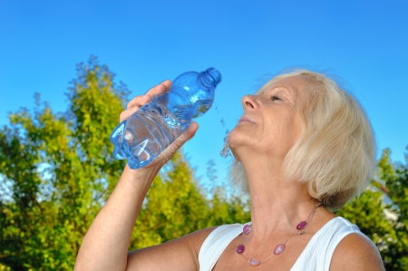 Mature, blonde woman drinking water from bottle in garden の写真素材