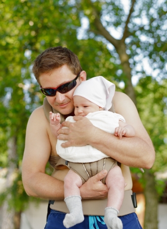 Happy father carries his baby in the carrier in sunny summer day の写真素材