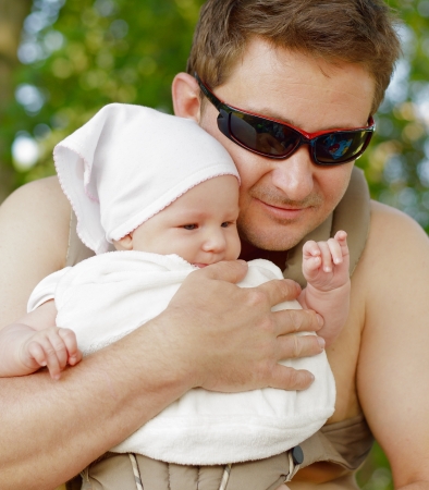 Happy father carries his baby in the carrier in sunny summer day の写真素材