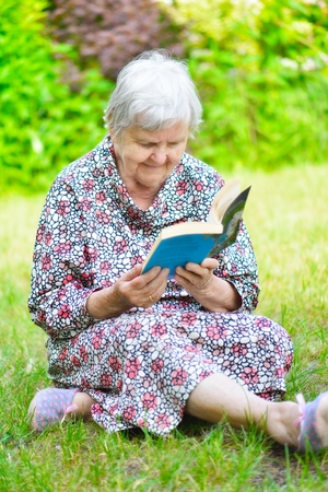 Senior woman reading book in park の写真素材