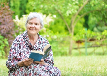 Senior woman reading book in park の写真素材