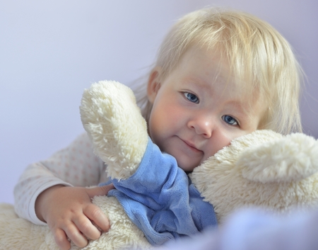 Cute baby with blue eyes hugging a mascot の写真素材