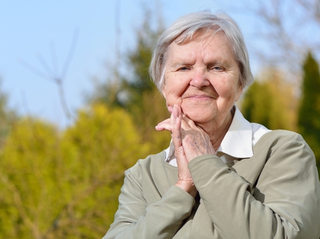 Senior woman looking and smiling in garden on blue sky.の写真素材