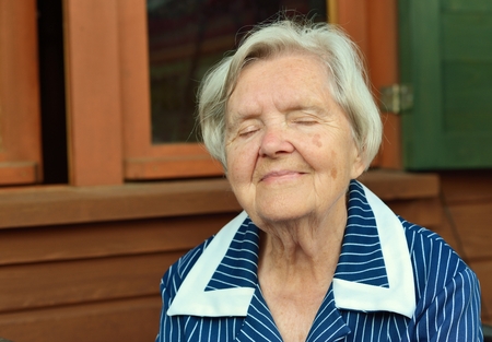 Senior smiling woman is sitting on terrace of the house.