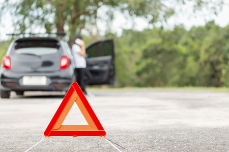 Red emergency stop sign with blurred car and woman calling car mechanic in the background