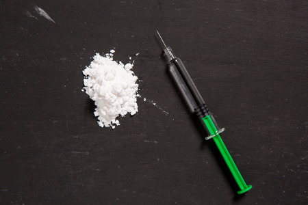 Cocaine drugs heap with syringe on a black background