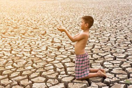 Child sit on cracked earth in the arid areaの写真素材
