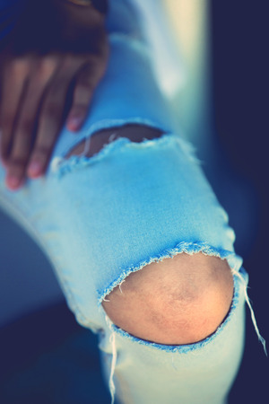 Closeup of tear in old worn out jeans in vintage toneの写真素材