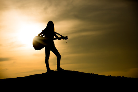 Silhouette of woman with guitar on the sunsetの写真素材