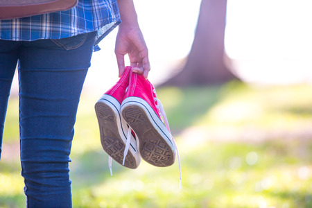 Barefoot woman walking on the grass with holding red shoesの写真素材