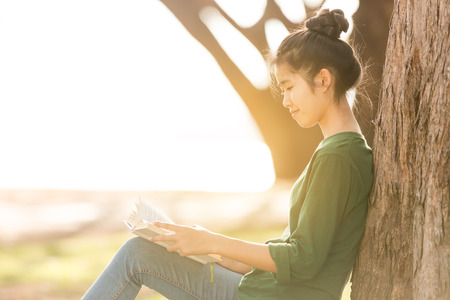 Beautiful young asian woman sitting and reading book in a park