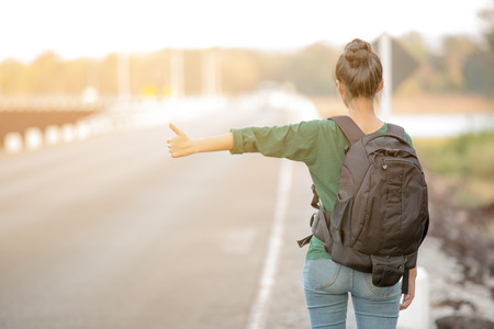 tourist girl with  backpack hitchhiking on the roadの写真素材