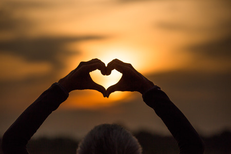Silhouette of happy young couple outdoors making  heart shape with handの写真素材