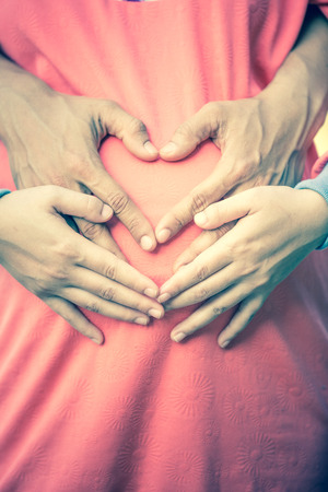 Pregnant Woman and Her Husband holding her hands in a heart shape on her baby bump.の写真素材