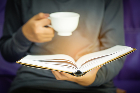 woman sitting on a sofa and reading a book while holding coffee cupの写真素材