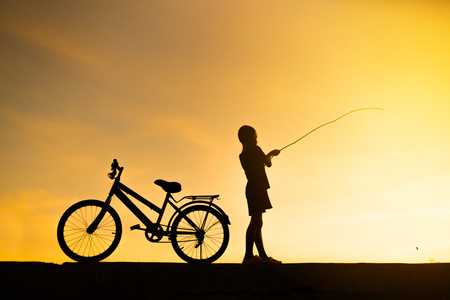 silhouette of  boy fishing and bicycle with sunset backgroundの写真素材