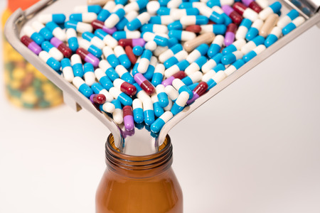 colorful medical drug capsule falling from medicaltray to browb bottle on white backgroundの写真素材