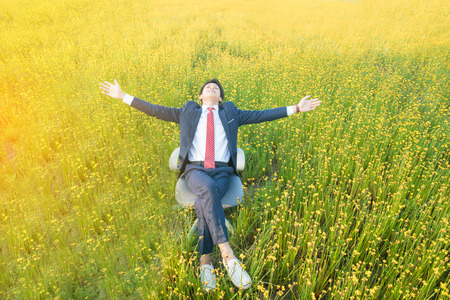 businessman sitting in office armchair and open arm in yellow flower field.Business concept in relaxationの写真素材