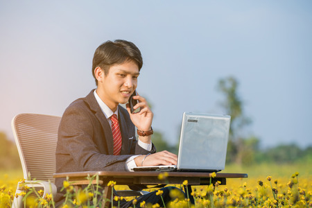 businessman using smartphone and laptop in yellow flower fieldの写真素材