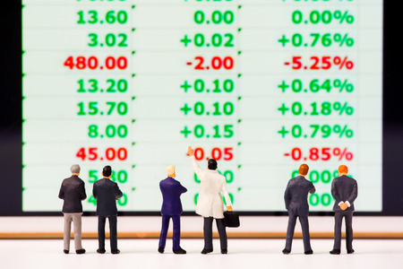 Miniature figure business people looking at stock board
