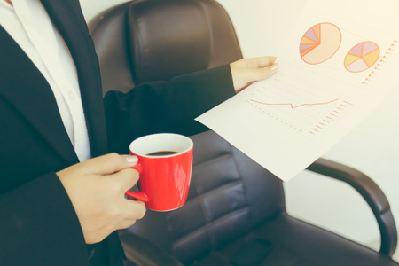 business woman holding data report chart while drinking coffeeの写真素材