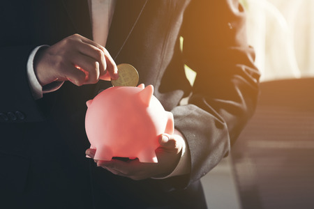 businessman hand putting coin into piggy bankの写真素材