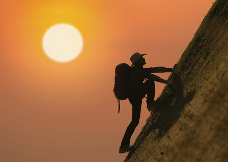 Silhouette of backpacker climbing on mountain at sunset or sunriseの写真素材