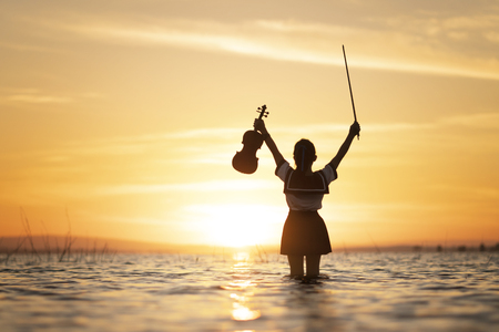 Girl playing violin on water with sunset backgroundの写真素材