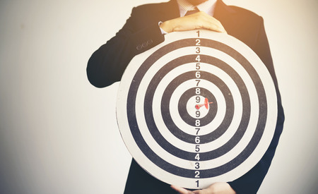 Businessman holding dartboard with a darts aiming at the target, business conceptの写真素材