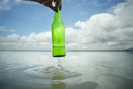 Close up hand picking up glass bottle in the lake , Drought and environmental problems and pollution concept.の写真素材
