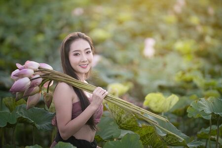 Woman holding lotus with traditional dressing in gardenの写真素材