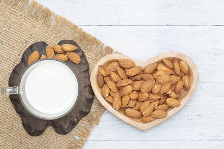 Cup of almond milk and nuts on heart shape wooden bowl on white wooden,top viewの写真素材