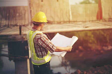 Engineer wear a hard hellmet and holding blueprint at construction siteの写真素材